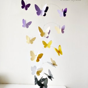May include: A mobile with butterflies in shades of purple, yellow, white, and gray. The butterflies are suspended from a wire frame and hang at different levels. The mobile is a whimsical and decorative piece for a nursery or child's room.