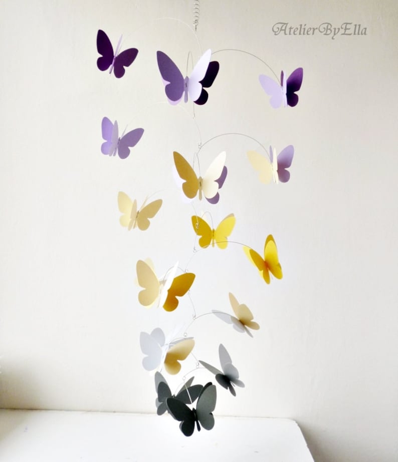 May include: A mobile with butterflies in shades of purple, yellow, white, and gray. The butterflies are suspended from a wire frame and hang at different levels. The mobile is a whimsical and decorative piece for a nursery or child's room.