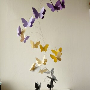 May include: A mobile with butterflies in shades of purple, yellow, and gray. The butterflies are suspended from a wire frame and are arranged in a spiral pattern.