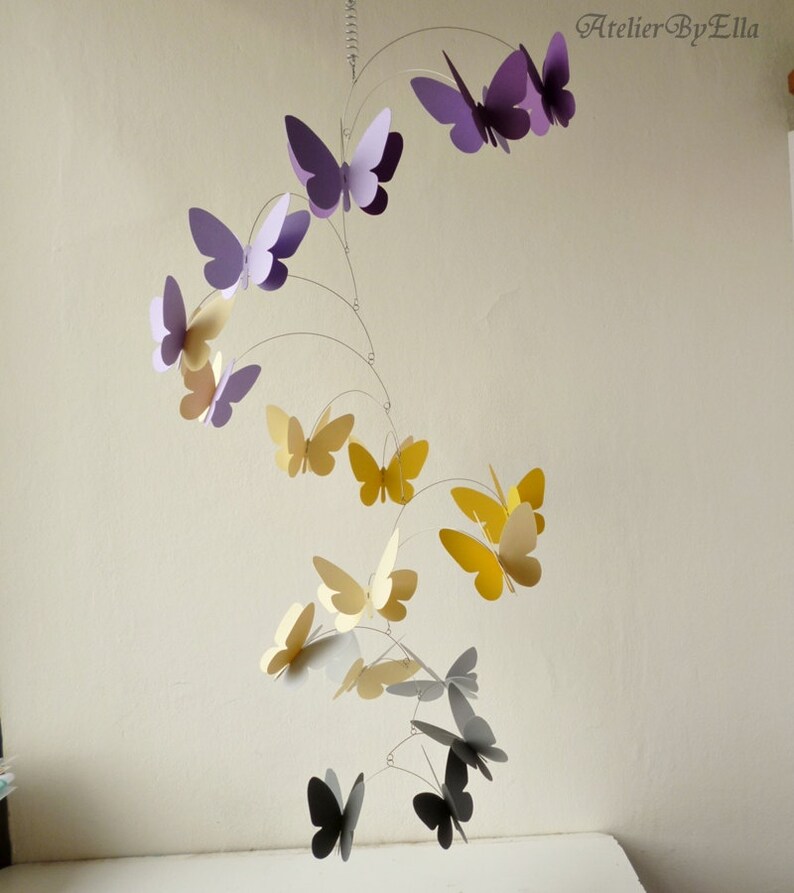 May include: A mobile with butterflies in shades of purple, yellow, and gray. The butterflies are suspended from a wire frame and are arranged in a spiral pattern.