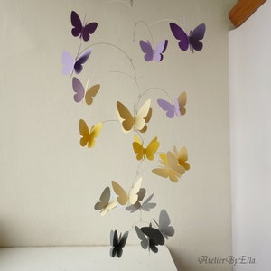 May include: A mobile with multiple paper butterflies in shades of purple, yellow, and gray hanging from a wire frame. The butterflies are arranged in a spiral pattern.