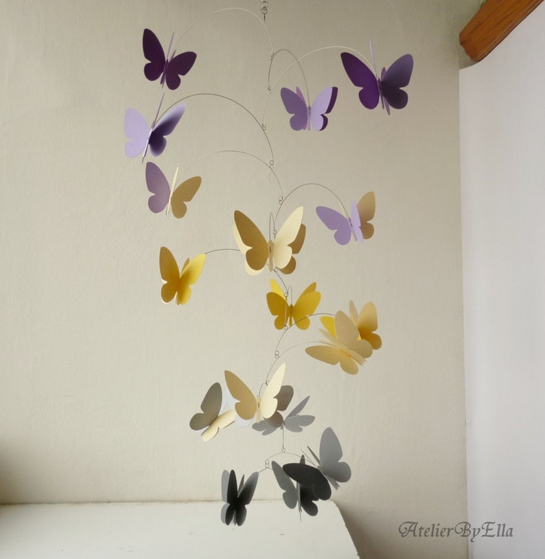 May include: A mobile with multiple paper butterflies in shades of purple, yellow, and gray hanging from a wire frame. The butterflies are arranged in a spiral pattern.