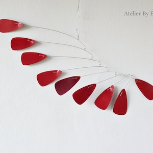 May include: A red mobile with 10 teardrop-shaped metal pieces hanging from a wire frame. The mobile is suspended from the ceiling.