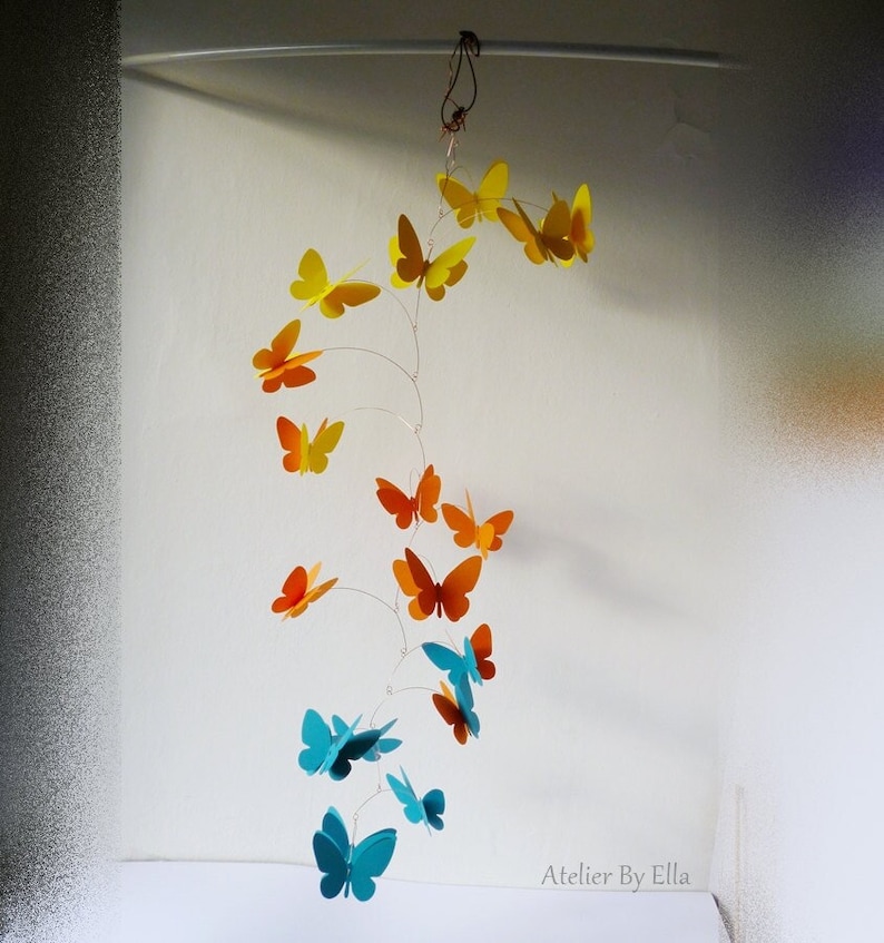 May include: A mobile with a spiral design featuring butterflies in shades of yellow, orange, and blue. The mobile is suspended from a white ceiling.