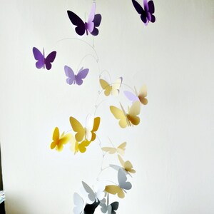 May include: A mobile with purple, yellow, and gray paper butterflies hanging from a wire frame. The butterflies are arranged in a cascading pattern, with the largest butterflies at the top and the smallest butterflies at the bottom.