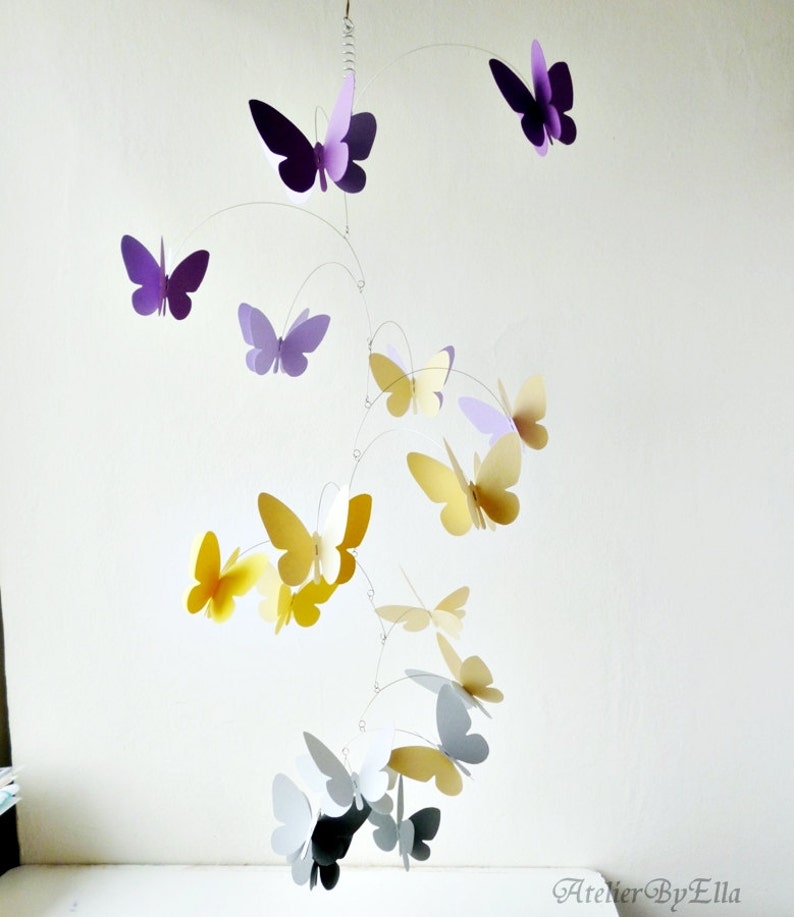 May include: A mobile with purple, yellow, and gray paper butterflies hanging from a wire frame. The butterflies are arranged in a cascading pattern, with the largest butterflies at the top and the smallest butterflies at the bottom.
