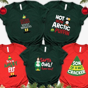 May include: Five short-sleeved t-shirts in dark green and red colors. The shirts feature various holiday-themed graphic prints with text including Cotton Headed Ninny Muggins, Not Now Arctic Puffin, He's an Angry Elf, Santa OMG I know him, and Son of a Nut Cracker.