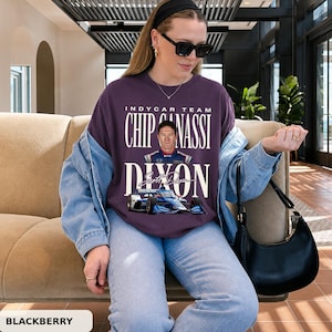 Może przedstawiać: Ciemnofioletowy t-shirt z krótkim rękawem z nadrukiem graficznym kierowcy IndyCar Scotta Dixona, napisem "INDYCAR TEAM CHIP GANASSI DIXON" oraz niebieskim samochodem wyścigowym. Koszulka jest noszona z jasnoniebieską kurtką dżinsową, jasnoniebieskimi dżinsami i czarną torebką.