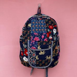 Peut inclure: Un sac à dos matelassé avec une base bleu foncé et un motif patchwork multicolore composé de fleurs, de tigres et de formes géométriques. Le sac comprend une poche avant avec une bordure rayée bleu et blanc, une poignée et deux bretelles.