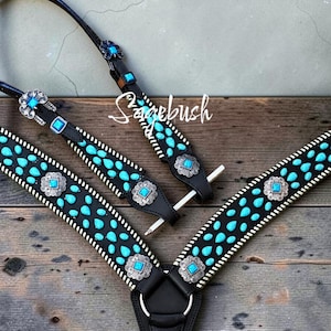 Puede incluir: Un conjunto de petral y cabezada para caballo en cuero negro con conchos de metal plateado, incrustaciones de turquesa cuadradas y numerosas piedras de turquesa en forma de lágrima. Las correas de cuero tienen costuras blancas y la palabra Sagebush.