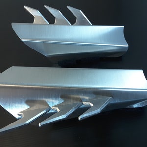 May include: Two silver metal pieces with a sharp, pointed design. The pieces are made of brushed metal and have a sleek, modern look.