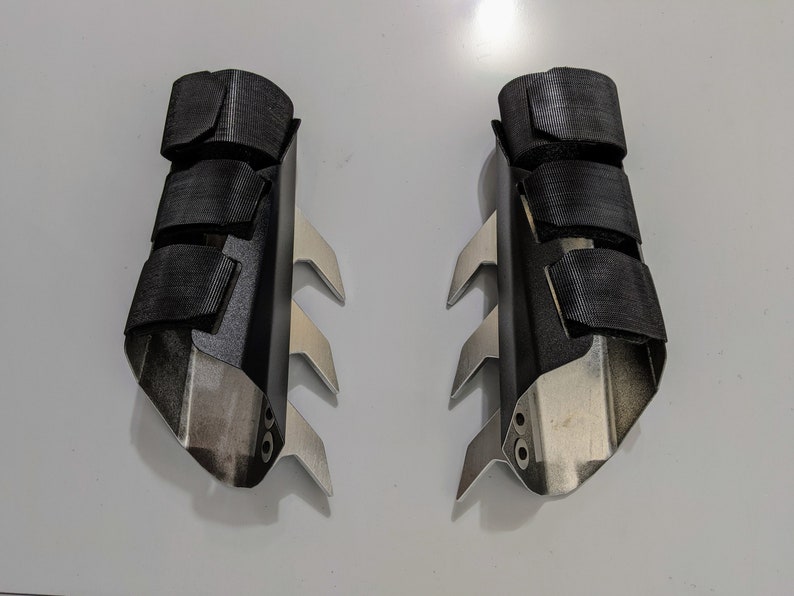 May include: A pair of black and silver cosplay gauntlets with a textured surface and sharp points.