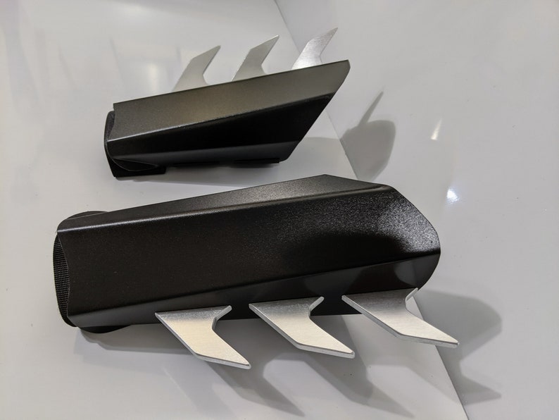 May include: A pair of black arm guards with silver claws. The guards are made of a textured material and have a sleek, modern design.