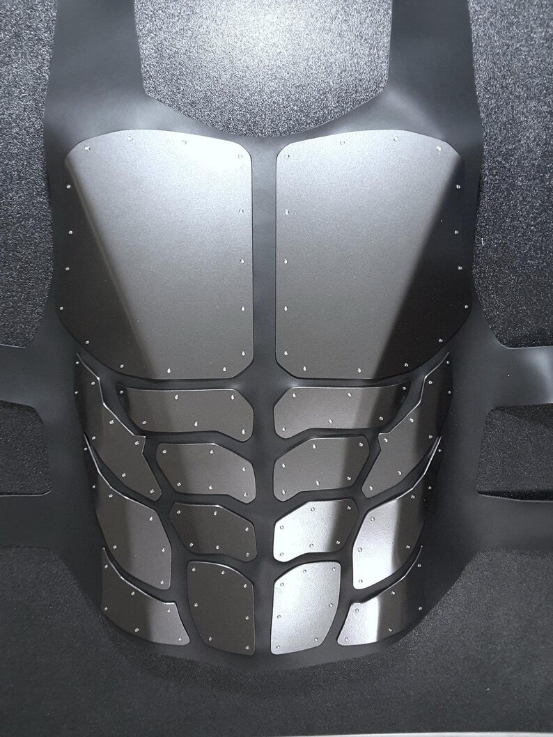 May include: A black and silver chest plate with a textured design. The chest plate is made of multiple pieces of metal that are connected by rivets.