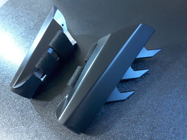 May include: Two black plastic pieces with sharp edges. One piece has a strap with a buckle. The pieces are designed to look like claws.