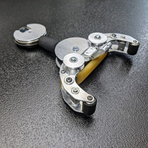 Könnte beinhalten: Eine silberne und schwarze mechanische Hand mit einer gelben Gummwalze. Die Hand ist aus Metall und hat eine Reihe von Zahnrädern und Rädern.