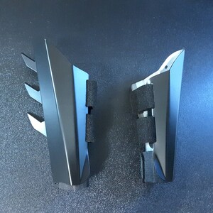 May include: Two black plastic pieces with a triangular shape and a textured surface. The pieces have a series of small, sharp points on one side.