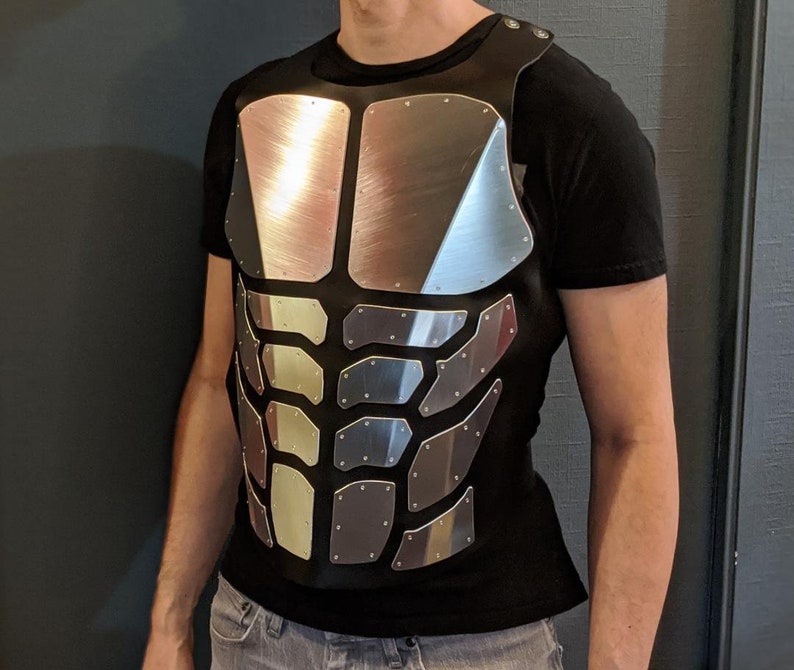 May include: A black shirt with a silver, segmented, chest plate design. The plate is made of multiple pieces that resemble a human torso.