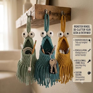 May include: Three hanging crochet organisers in sage green, teal, and mustard yellow, each featuring two large white eyes and a fringed bottom. They hang from a wooden shelf, holding items like charger cables, pens, and keys. Text reads: MONSTER MINDS: DE-CLUTTER YOUR DESK & ENTRYWAY, CHARGER CABLES, PENCILS & PENS, KEYS & SMALL ITEMS, CUSTOM COLORS.