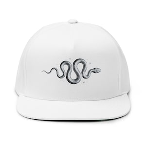 Può includere: Un cappellino snapback bianco con un'illustrazione dettagliata in bianco e nero di un serpente in una posizione sinuosa a forma di S, centrata sul pannello frontale. Il cappello presenta una corona strutturata e una visiera piatta.