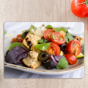 May include: A close-up of a salad with croutons, tomatoes, olives, and basil on a white plate. The salad is on a wooden surface.