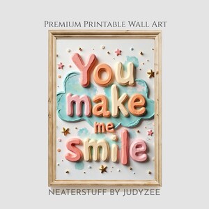 May include: A framed print featuring the phrase "You make me smile" in 3D lettering. The letters are in pink, orange, and cream, set against a light blue cloud. The frame is light wood, with star accents. The art is by Neaterstuff by Judyzee.
