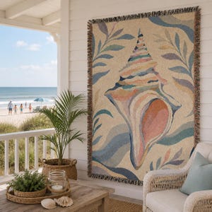 May include: A rectangular woven throw blanket featuring a large central seashell graphic in shades of pink, blue, and tan, surrounded by stylized leaf patterns and wavy lines. The blanket has a fringed edge and a textured, multi-colored appearance.
