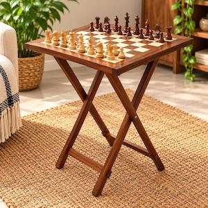 May include: A wooden folding table with a square top featuring an integrated chessboard. The board has alternating light and dark squares, with a full set of light and dark wooden chess pieces arranged in their starting positions on the surface.