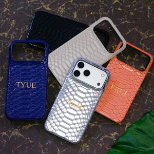 May include: A collection of five smartphone cases featuring a textured snakeskin pattern. The cases are available in blue with the text TYUE, black, cream, orange with the text ERH, and a silver case with the text G.R. Each case has a camera cutout.