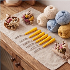 May include: Six seam rippers with bright yellow handles and silver metal tips arranged in a row, accompanied by four balls of yarn in cream, light blue, and mustard yellow, along with two small bouquets of dried flowers wrapped in brown paper.