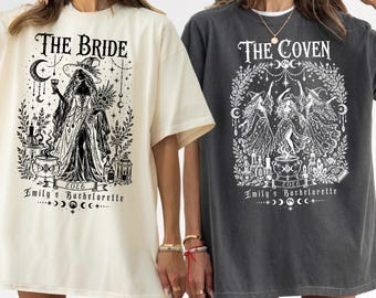 May include: Two short-sleeve t-shirts, one cream and one charcoal gray, featuring black and white graphic prints. The cream shirt displays a witch with the text THE BRIDE and Emily's Bachelorette 2026. The gray shirt shows three witches with THE COVEN.