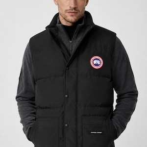 May include: A black quilted vest featuring a high collar, a front snap-button closure, and two large lower pockets. A circular Canada Goose patch is on the left chest, and a small Canada Goose label is stitched onto the lower right pocket.