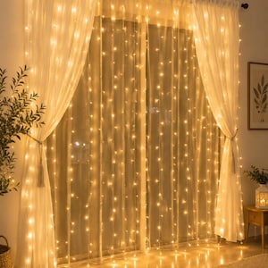 May include: A set of warm white LED curtain string lights hanging vertically in front of sheer white curtains. The lights are arranged in multiple parallel strands, creating a glowing backdrop that illuminates the fabric with a soft, golden light.