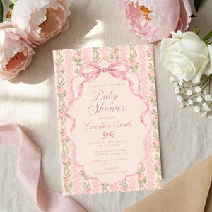 May include: A rectangular baby shower invitation card featuring a pale pink background with vertical stripes of pink roses and green vines. A central pink ribbon bow frames the text, which reads: Please join us for a Baby Shower honoring Caroline Smith.