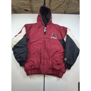 May include: A maroon, black, and white hooded jacket with a full-length front zipper. The jacket features a logo on the upper left chest with the letter A and the text Arizona. It has long sleeves with color-blocked panels and ribbed cuffs.