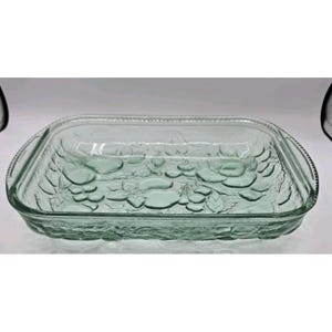 May include: A rectangular clear glass baking dish featuring an embossed fruit and leaf pattern on the bottom. The dish has integrated handles on both ends with a beaded rim detail along the edges of the handles and the top perimeter.