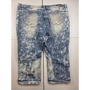 May include: Blue and white acid-wash denim capri pants featuring a mid-rise waist, a button and zipper closure, and two back pockets. Each back pocket is shaped like an apple and decorated with intricate embroidery and small silver studs.