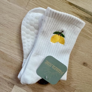 May include: White ankle socks with a yellow lemon embroidery and green leaves. The socks have a non-slip grip on the bottom and a tag that reads "PARKER JUNE".