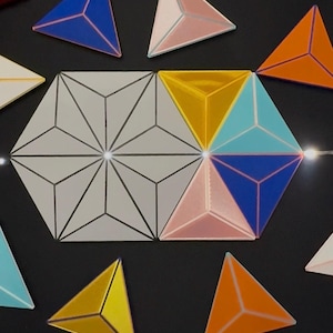 Peut inclure: Une collection de tuiles géométriques comprenant un grand assemblage hexagonal de triangles blancs et plusieurs tuiles triangulaires individuelles en bleu, orange, jaune, bleu clair et rose. Les tuiles présentent des lignes centrales en relief.