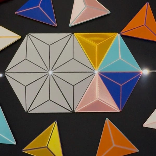 May include: A collection of geometric tiles including a large hexagonal assembly of white triangles and several individual triangular tiles in blue, orange, yellow, light blue, and pink. The tiles feature raised central lines and smooth surfaces.