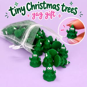 May include: A collection of miniature green Christmas tree figurines with white eyes and raised middle fingers, spilling out of a sheer white organza drawstring bag. The text tiny Christmas trees gag gift is displayed at the top of the image.