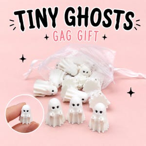 May include: A collection of small white ghost figurines with black eyes and raised middle fingers, packaged in a sheer white drawstring bag. The text TINY GHOSTS GAG GIFT is displayed at the top. Each ghost has a scalloped base and smooth finish.