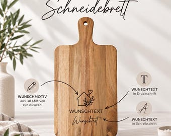 Könnte beinhalten: Ein rechteckiges Holzschneidebrett mit Griff und Aufhängeloch. Das Brett zeigt eine Lasergravur eines Haussymbols mit Herz und Blättern sowie den Text WUNSCHTEXT in Druck- und Schreibschrift, ergänzt durch die Überschrift DEIN INDIVIDUELLES Schneidebrett.