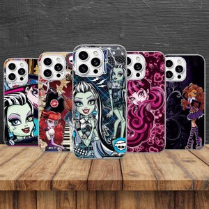 May include: Five smartphone cases featuring Monster High character illustrations. The designs include Frankie Stein with black and white hair, Draculaura with pink hair and heart patterns, and Clawdeen Wolf, all displayed on a wooden surface.