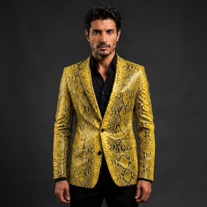 Puede incluir: Un blazer de color amarillo vibrante con un patrón detallado de piel de serpiente negra en toda la prenda. La chaqueta incluye solapas de muesca, dos botones frontales y dos bolsillos con solapa. Se lleva sobre una camisa negra de manga larga.