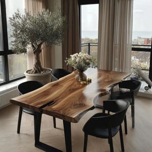 Peut inclure: Une table à manger rectangulaire avec un plateau en bois massif à bord naturel, présentant des motifs de grain brun et une fissure centrale sombre. La table est soutenue par des pieds en métal noir et entourée de quatre chaises noires.