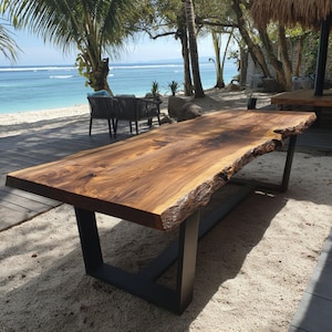 Puede incluir: Una mesa de comedor rectangular con un tablero grueso de madera marrón pulida con bordes naturales e irregulares. La mesa está sostenida por una estructura de metal negro resistente con dos patas rectangulares unidas por un travesaño central.