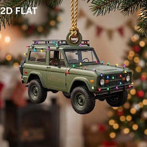 May include: A flat, olive green SUV Christmas tree ornament featuring a roof rack, black tires, and a string of multicolored holiday lights draped over the body. The name William is printed on the side door, and a gold cord is attached to the top.