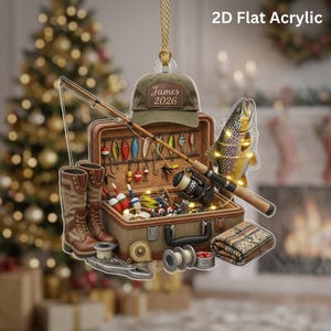 May include: A 2D flat acrylic ornament featuring a fishing theme with a brown tackle box, a fishing rod, a pair of brown boots, a trout, and a green baseball cap with the text James 2026. The design includes various fishing lures and gear.