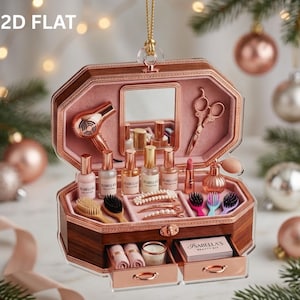 May include: A wooden beauty kit ornament featuring a rose gold hair dryer, scissors, perfume bottles, lipstick, hairbrushes, and clips. The interior includes a mirror and two small drawers with the text Isabella's Beauty Kit on a small card.